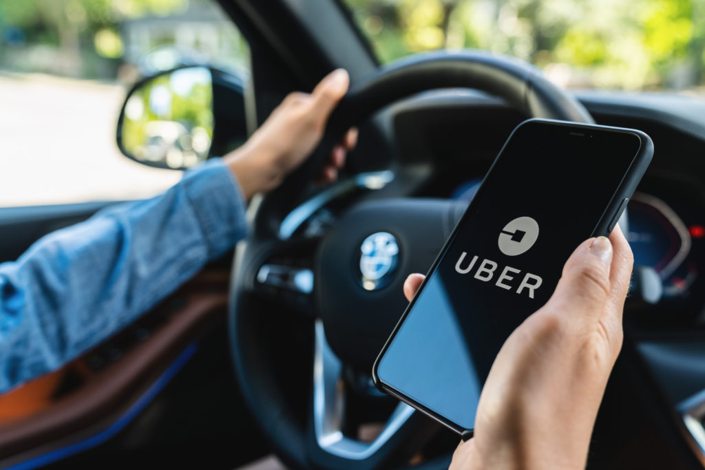 Uber driver holding smartphone in car. Uber is an American company offering transportation services online.